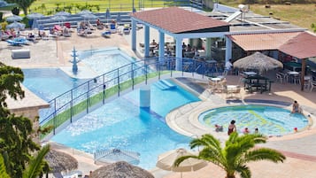 Zona de piscina de un complejo turístico con varias piscinas, sillas de descanso, sombrillas y mesas de comedor.