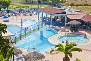 Zona de piscina de un complejo turístico con varias piscinas, sillas de descanso, sombrillas y mesas de comedor.