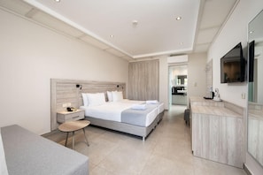 A modern hotel room with a large bed, a bedside table, a small round table, a built-in desk, and a TV mounted on the wall. - Palladium Hotel (KOS)