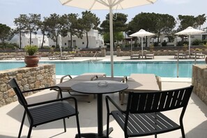 A poolside area with a table and chairs, a potted plant, and umbrellas. - Palladium Hotel (KOS)