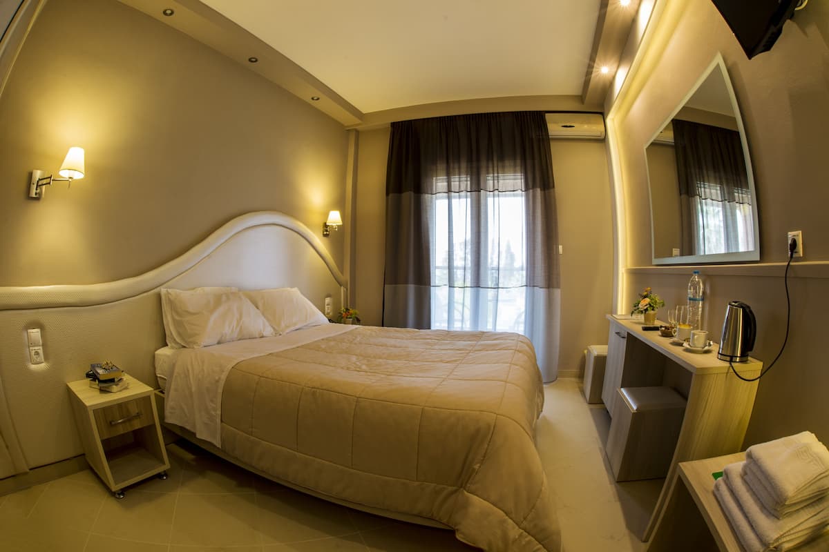 Ein Hotelzimmer mit einem großen Bett, Nachttischen, einem Schreibtisch mit Spiegel und einem Fenster mit Vorhängen.