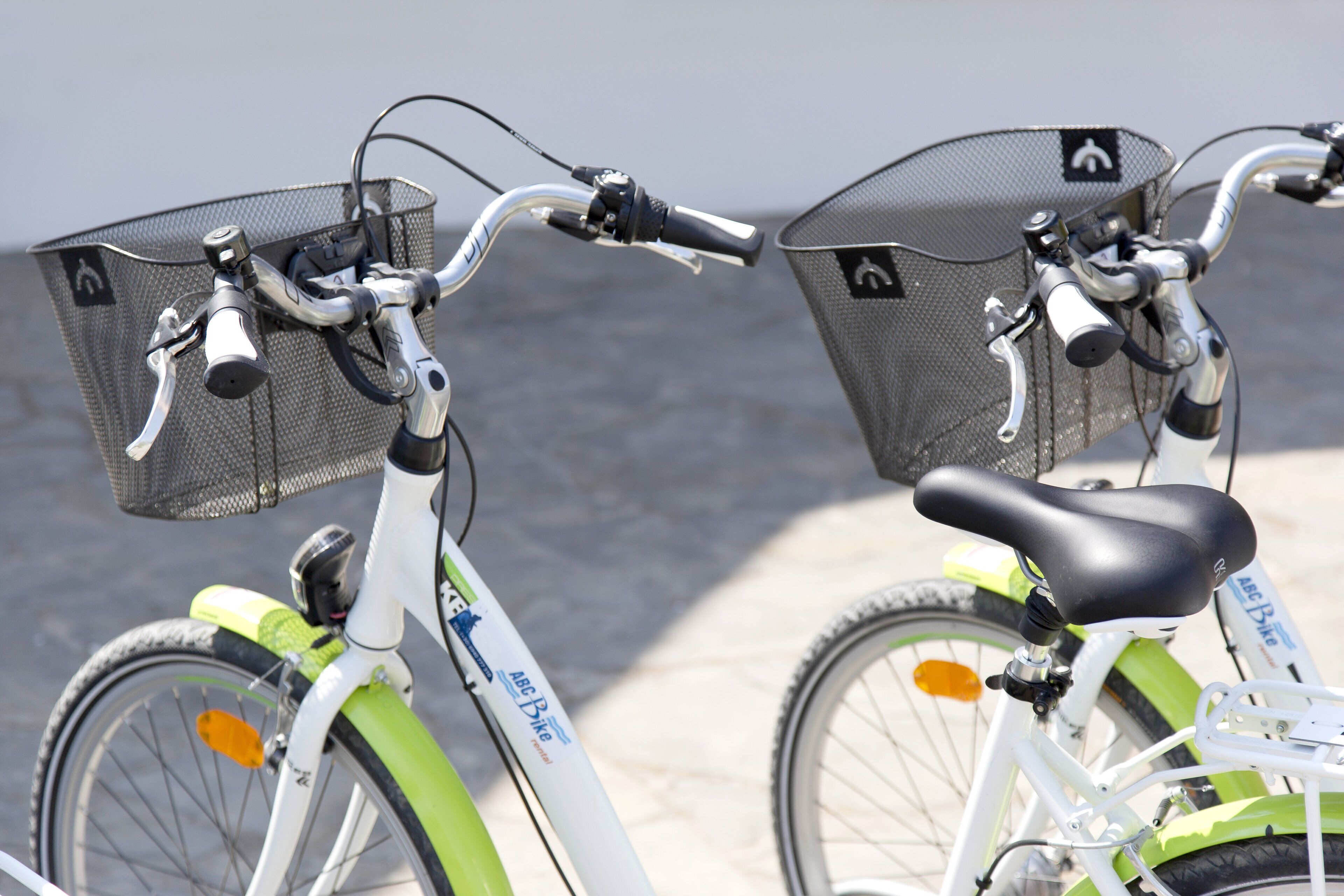 Duas bicicletas com cestas e um banco, estacionadas em um pavimento.