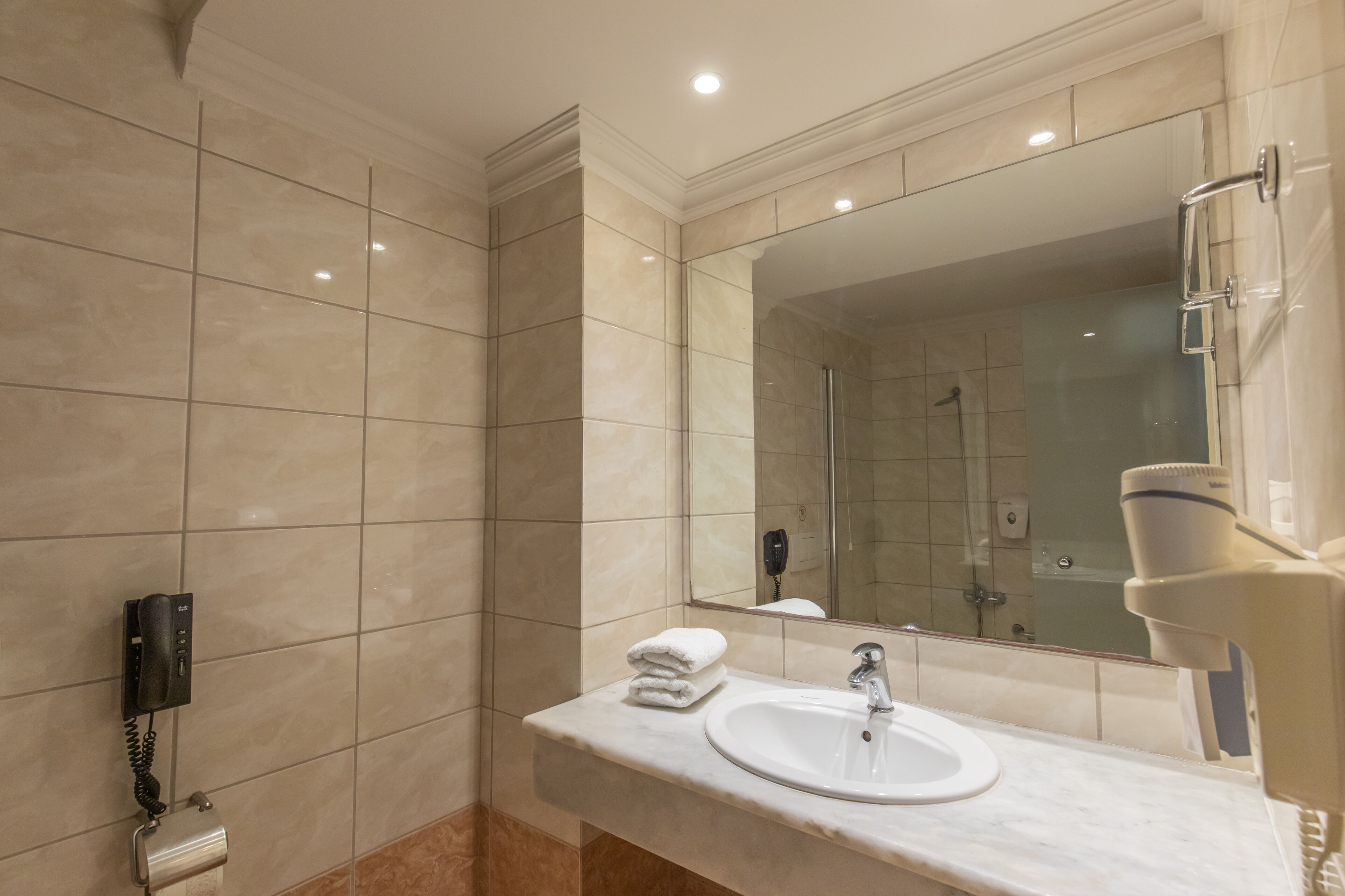 A bathroom with a marble-tiled wall, a sink with a mirror, a towel dispenser, and a telephone.