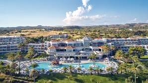 Resort com vários edifícios, uma piscina central e palmeiras.