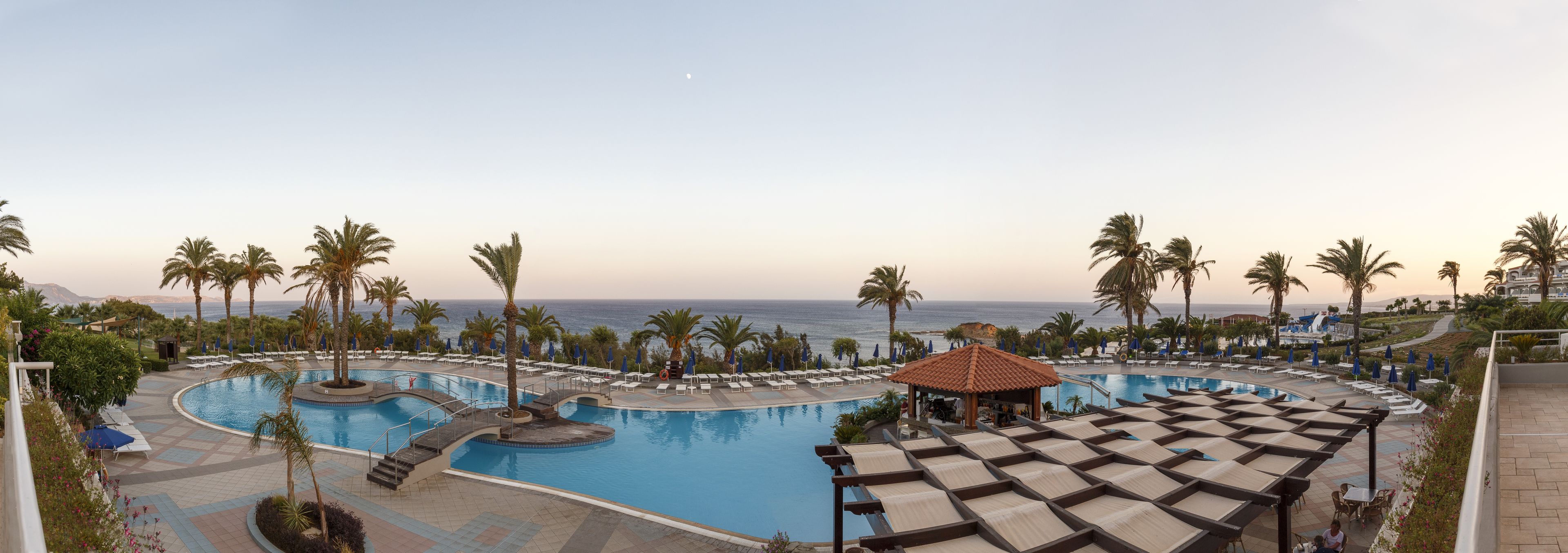 A resort pool area with multiple swimming pools, lounge chairs, and palm trees.