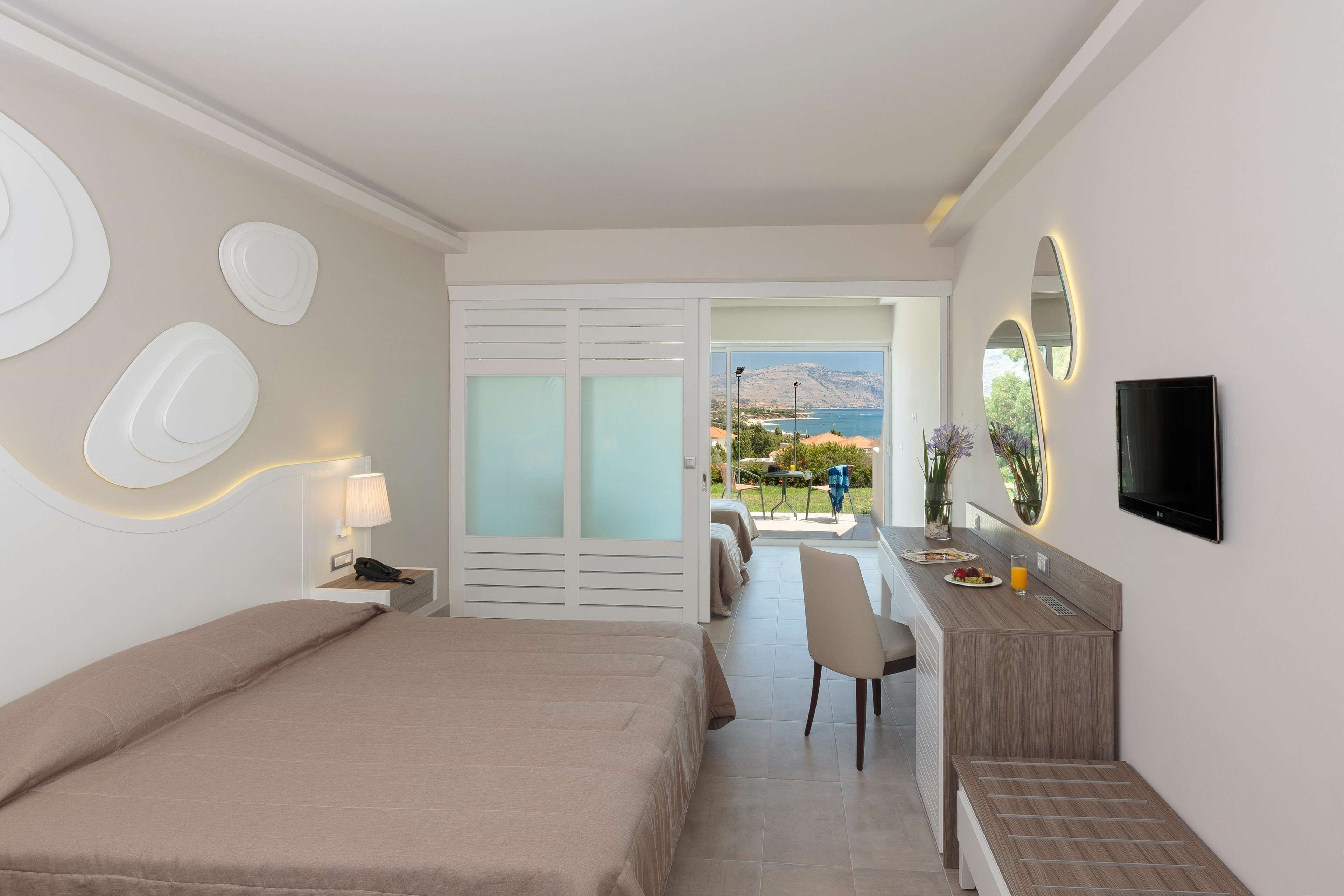 A hotel room with a bed, a desk, a chair, a TV, and a view of the outdoors.