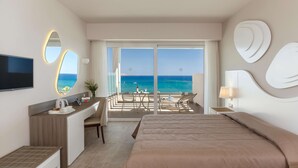 Quarto de hotel com cama, escrivaninha com televisão, varanda e vista para o mar, e um espelho grande.