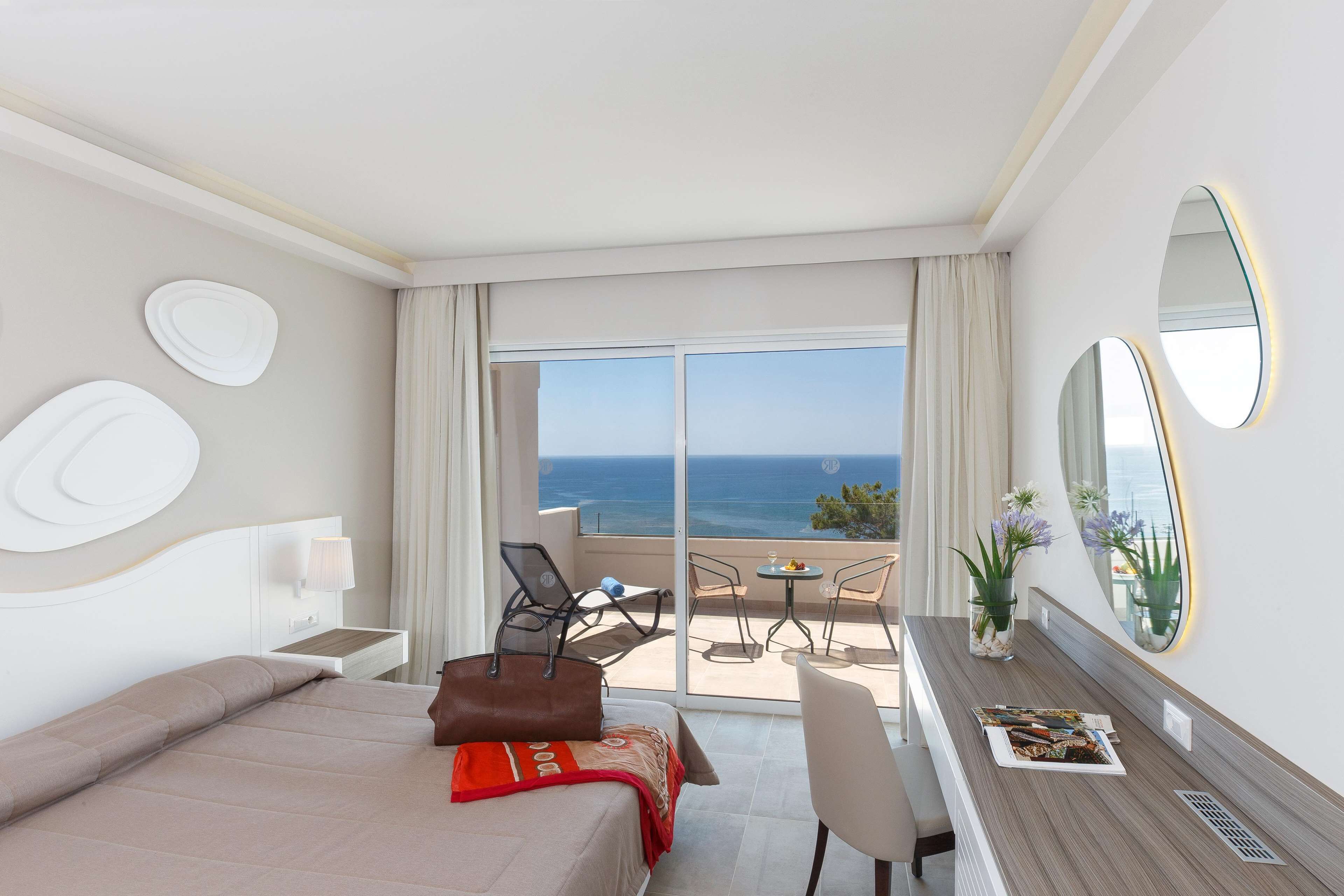 A hotel room with a bed, a desk, a chair, and a balcony with a view of the ocean.