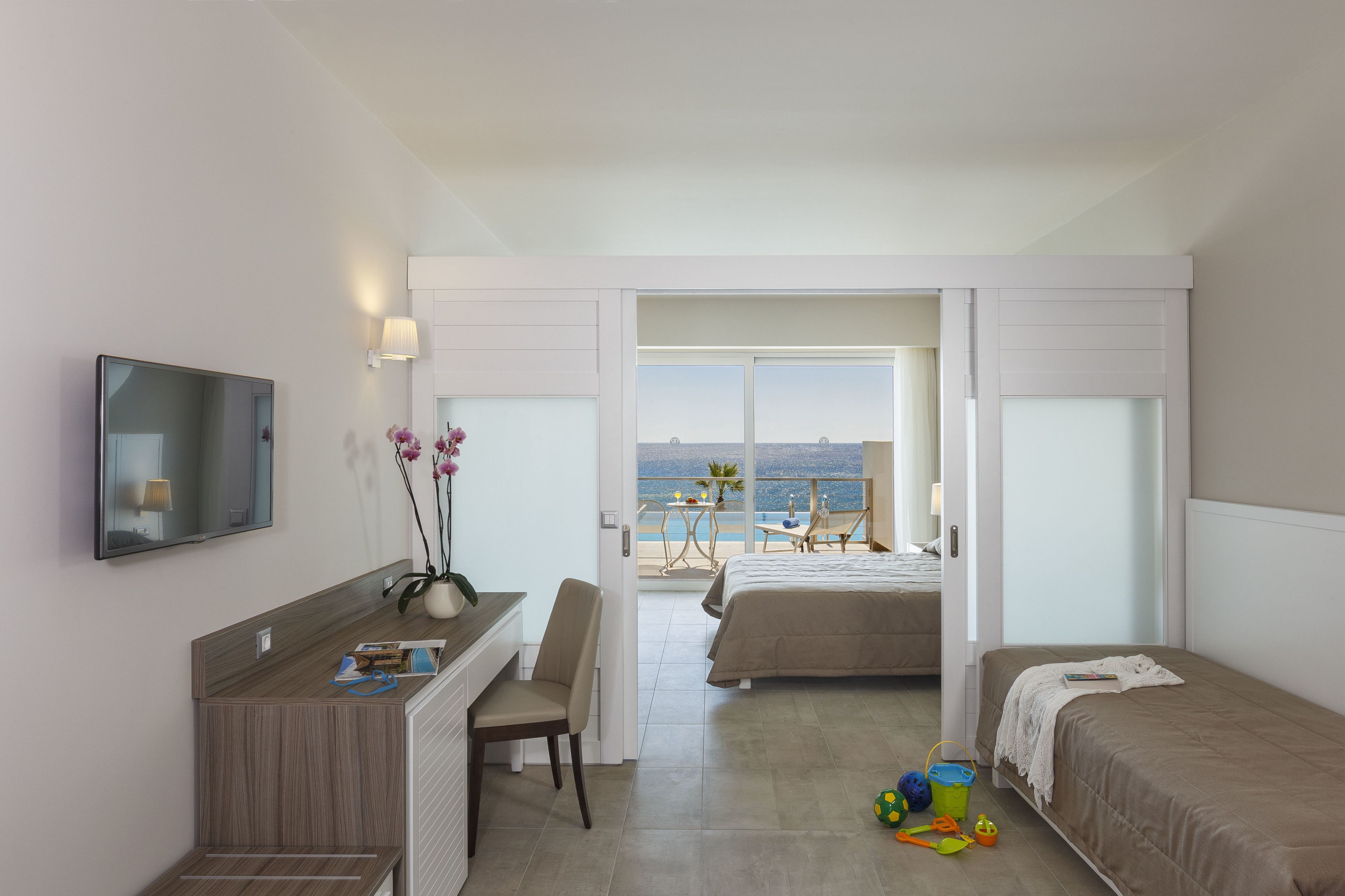 A hotel room with a desk, chair, and a bed. There is a view of the beach through the window.