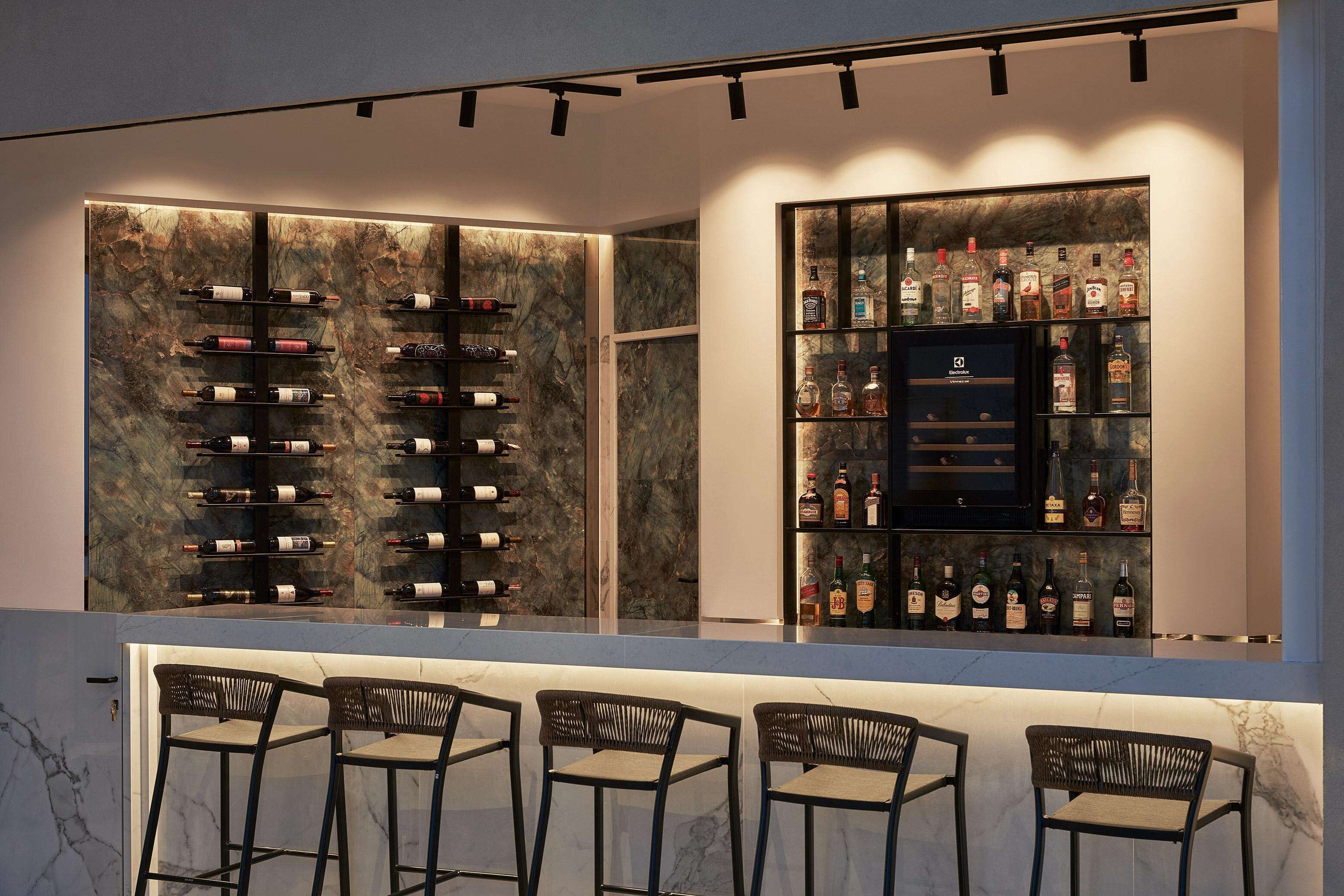 A bar area with a wine and liquor display, marble countertops, and four bar stools.