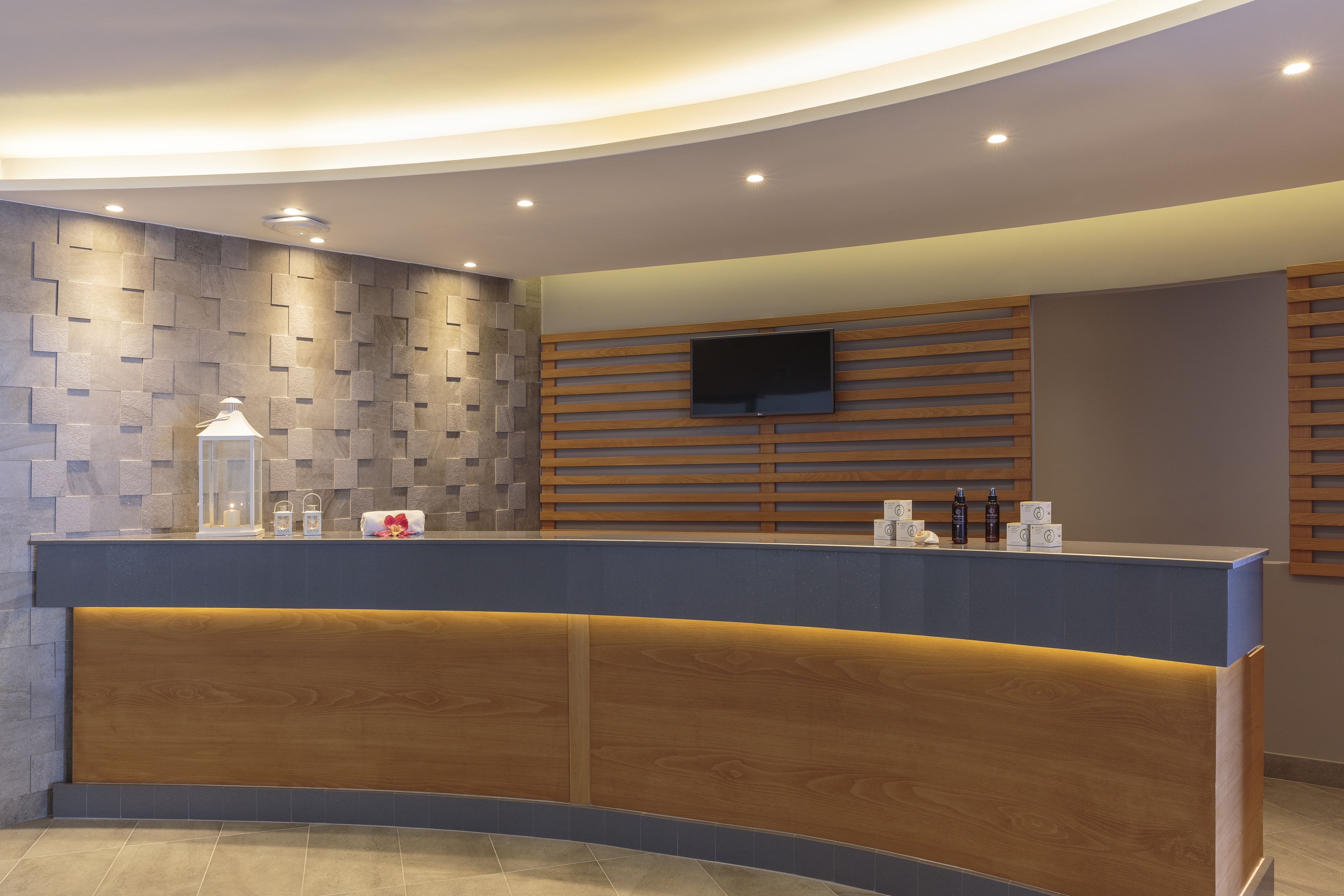 A reception area with a curved counter, a mounted TV, and a wooden panel wall.