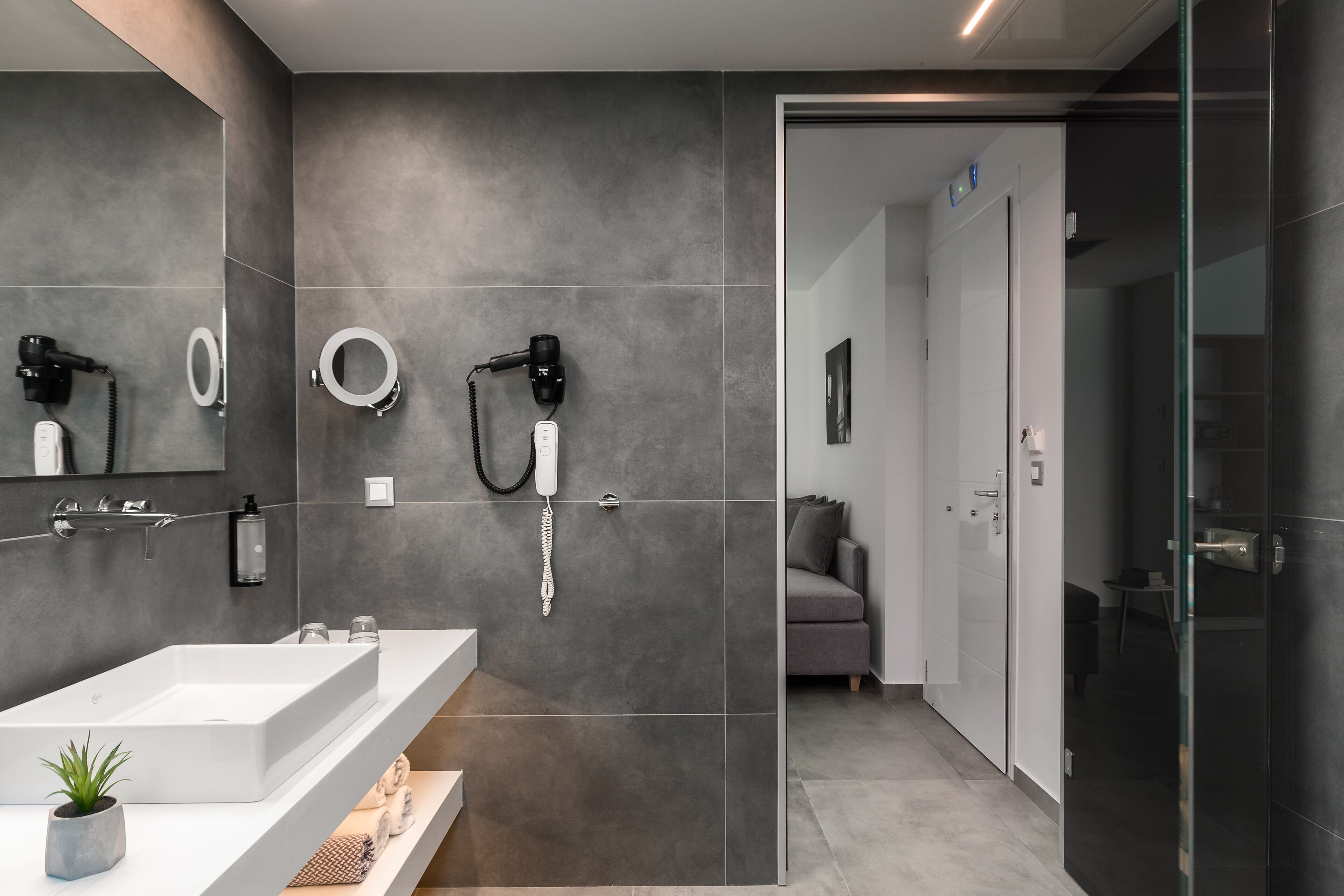 A modern bathroom with a large white sink, two hair dryers mounted on the wall, and a glass shower enclosure.