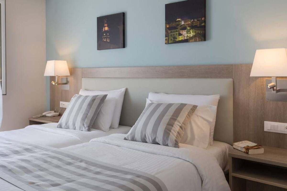 Una habitación de hotel con una cama grande, dos mesitas de noche y una ventana con cortinas.