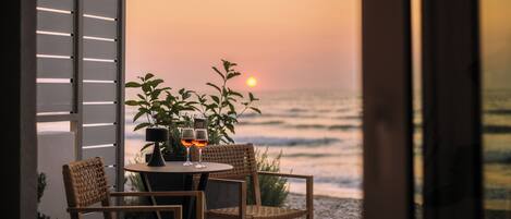 A table with two chairs and two glasses of red wine, overlooking the ocean at sunset.