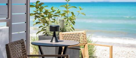 A patio with a table and chairs, overlooking a beach with clear blue water.