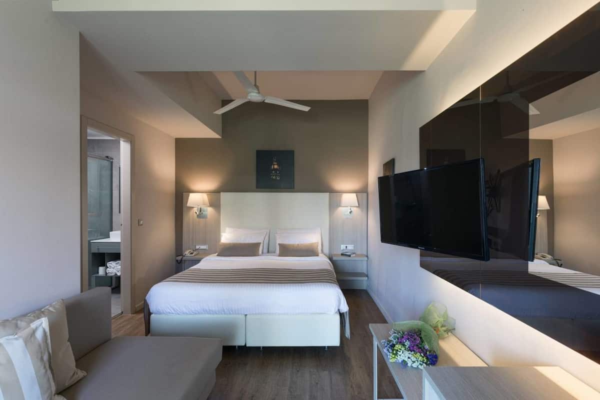 Habitación de hotel moderna con una cama grande, un televisor de pantalla plana, un ventilador de techo y un pequeño escritorio con un jarrón de flores.
