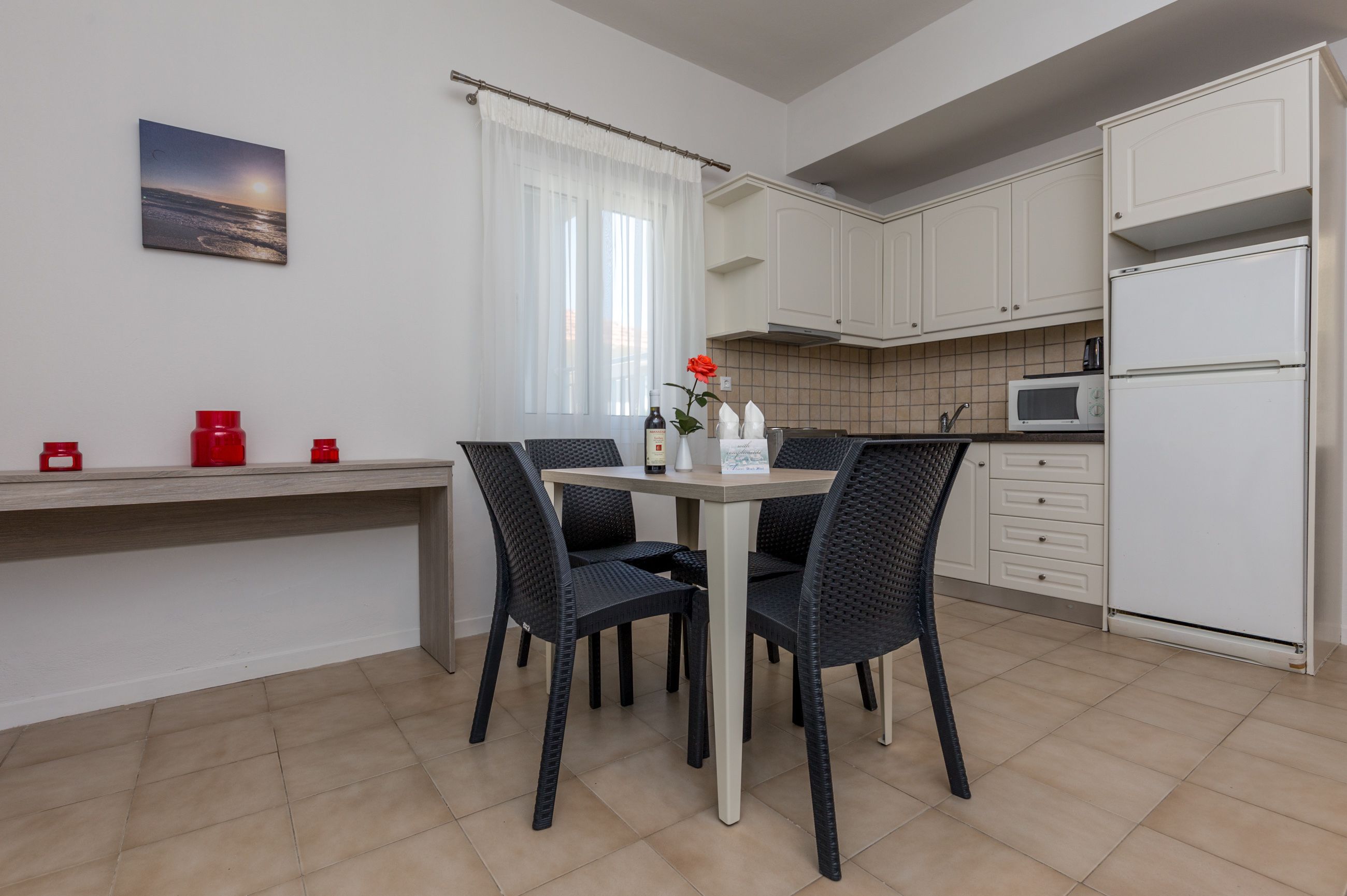 A modern kitchen with white cabinets, a dining table with chairs, a microwave, and a refrigerator.