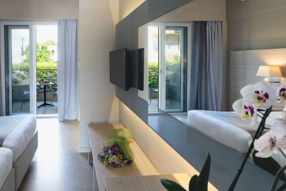 Una habitación de hotel moderna con dos camas, un televisor de pantalla plana, un balcón con una mesa y un arreglo floral.