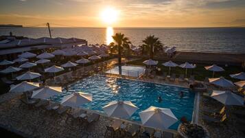 A poolside area with umbrellas and lounge chairs, overlooking a body of water at sunset.