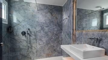 Un baño moderno con ducha de vidrio, un lavamanos blanco y paredes de mármol.