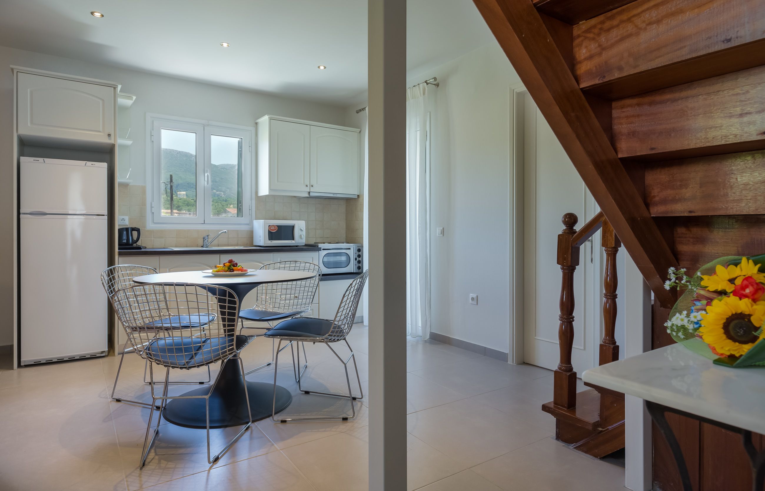 A modern kitchen with white cabinets, a refrigerator, a microwave, and a dining area with a round table and wire chairs.