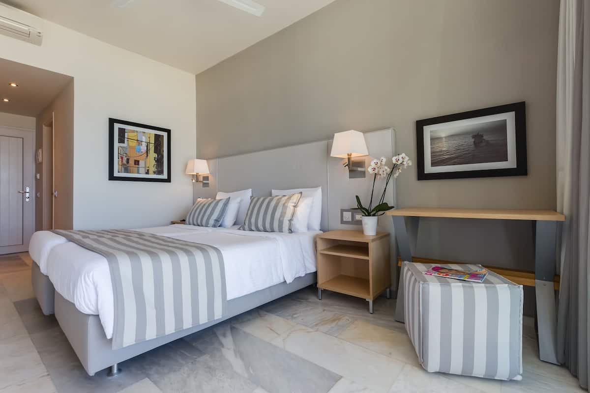 Un dormitorio de hotel moderno con una cama grande, lámparas de noche, una mesita y un cuadro enmarcado en la pared.