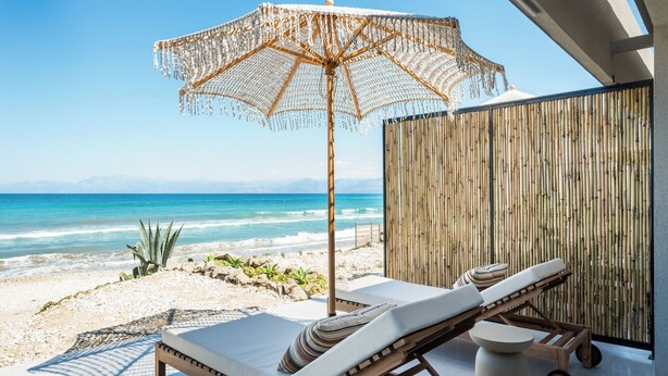 Un espacio de relax en la playa con una silla de madera y un paraguas tejido, con vistas al océano.