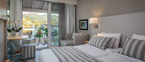 A hotel room with a bed, a chair, a small table with a vase of flowers, a lamp, and a view of the outside.