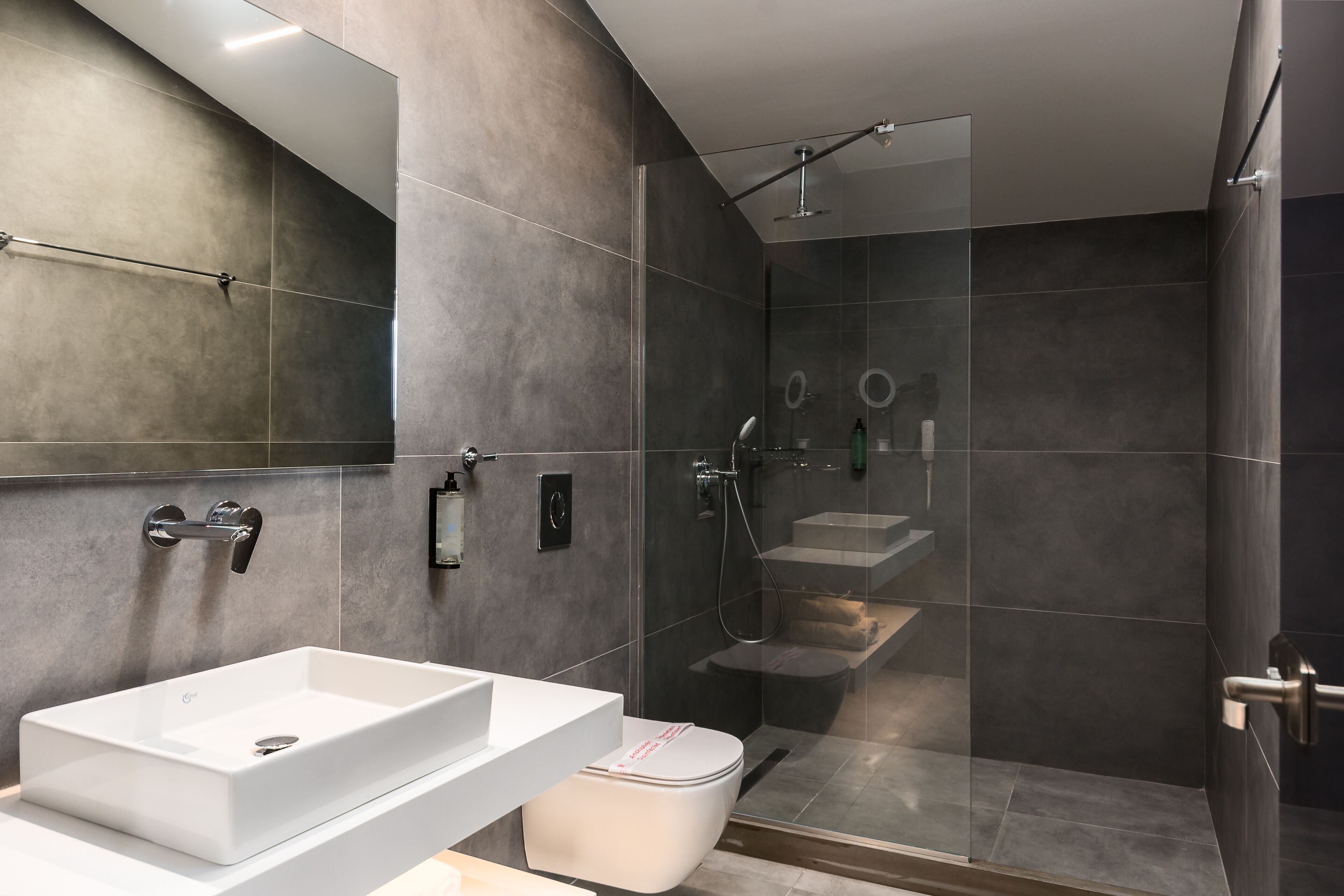 A modern bathroom with a large white sink, a toilet, and a glass-enclosed shower area.