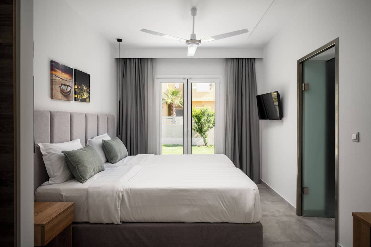 Ein modernes Schlafzimmer mit einem Bett, einem Deckenventilator, einem Fernseher und einer Schiebetür zum Außenbereich.