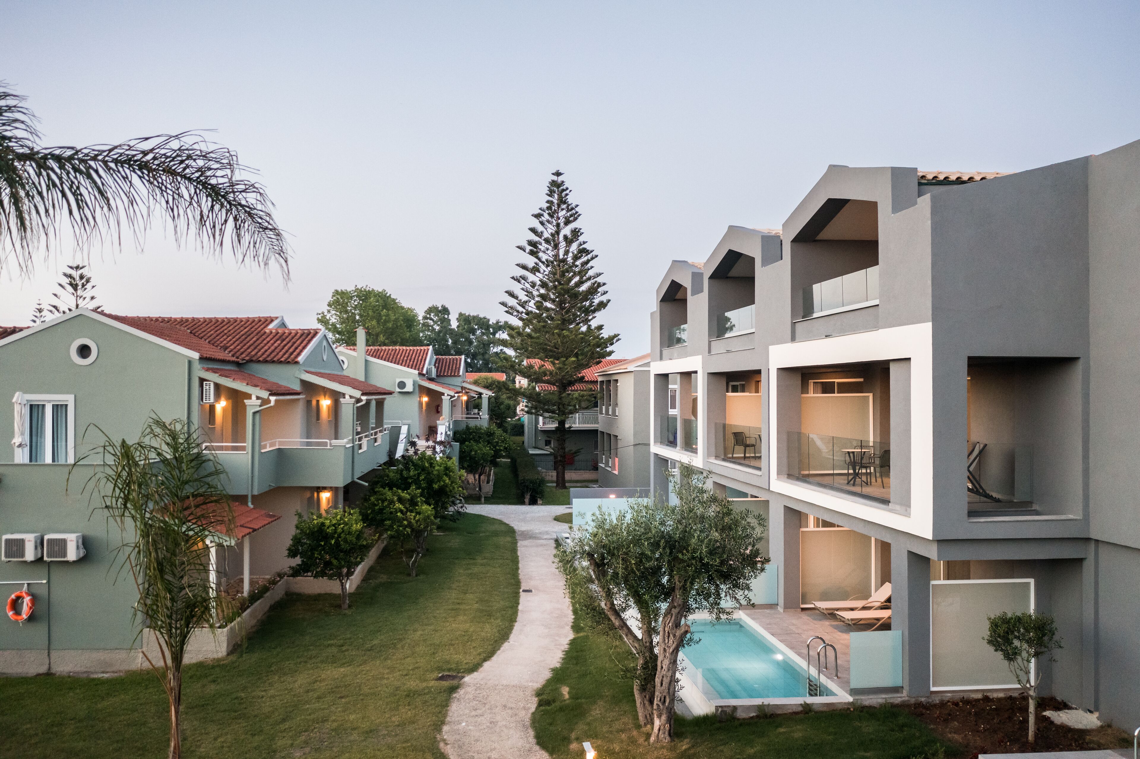 A modern hotel with multiple buildings, a swimming pool, and a well-maintained garden.