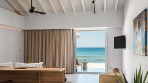 Una habitación moderna con un escritorio de madera, una silla, un ventanal con vista a la playa y un televisor instalado en la pared.