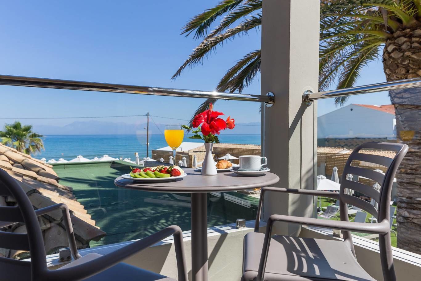 A balcony with a table set for breakfast, overlooking a pool and the sea.
