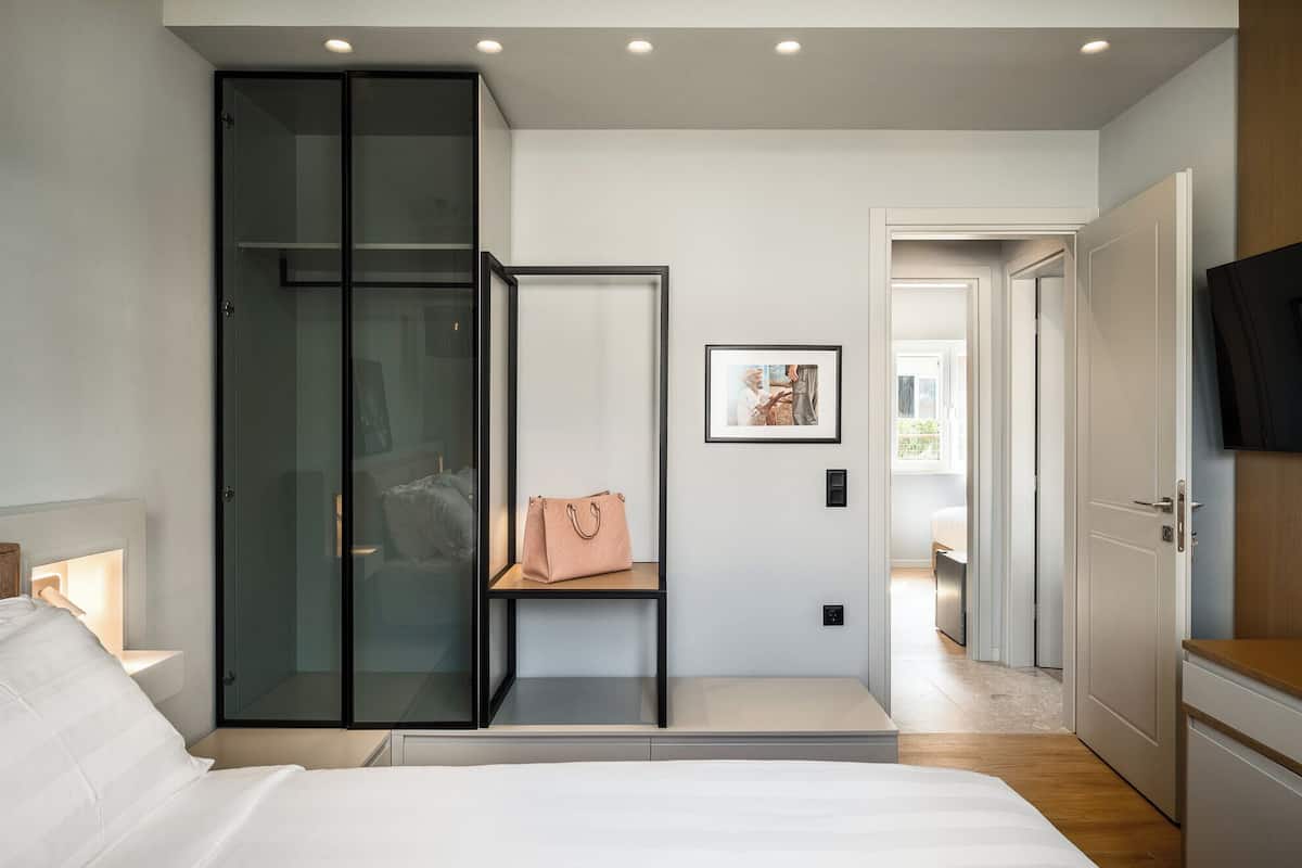 Ein modernes Schlafzimmer mit einem großen Bett, einem Schiebe-Glas-Schrank, einem gerahmten Bild an der Wand und einem an der Wand befestigten Fernseher.
