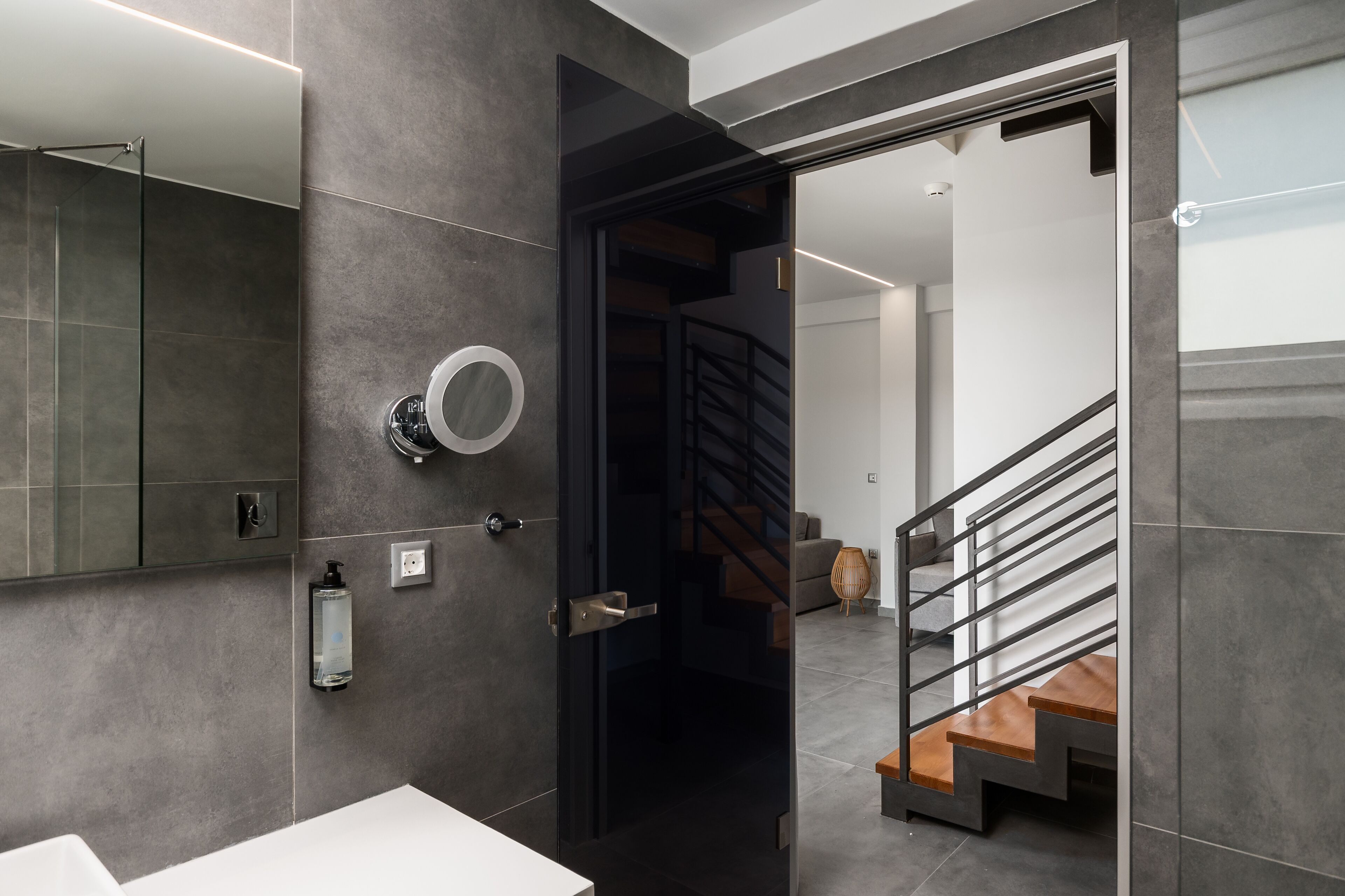 A modern bathroom with a large mirror, a round mirror, and a soap dispenser.