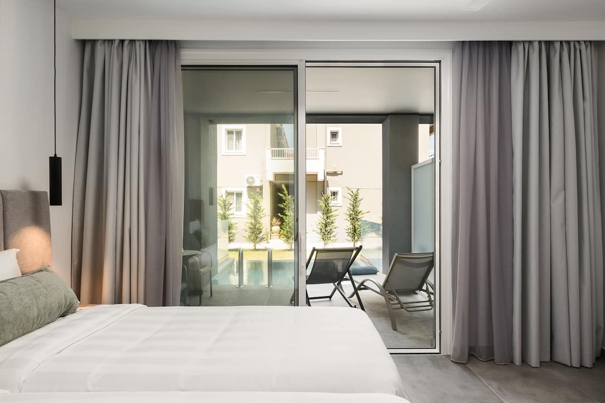 Ein modernes Hotelzimmer mit einem großen Bett, einer Schiebetür zu einem Balkon und Blick ins Freie.