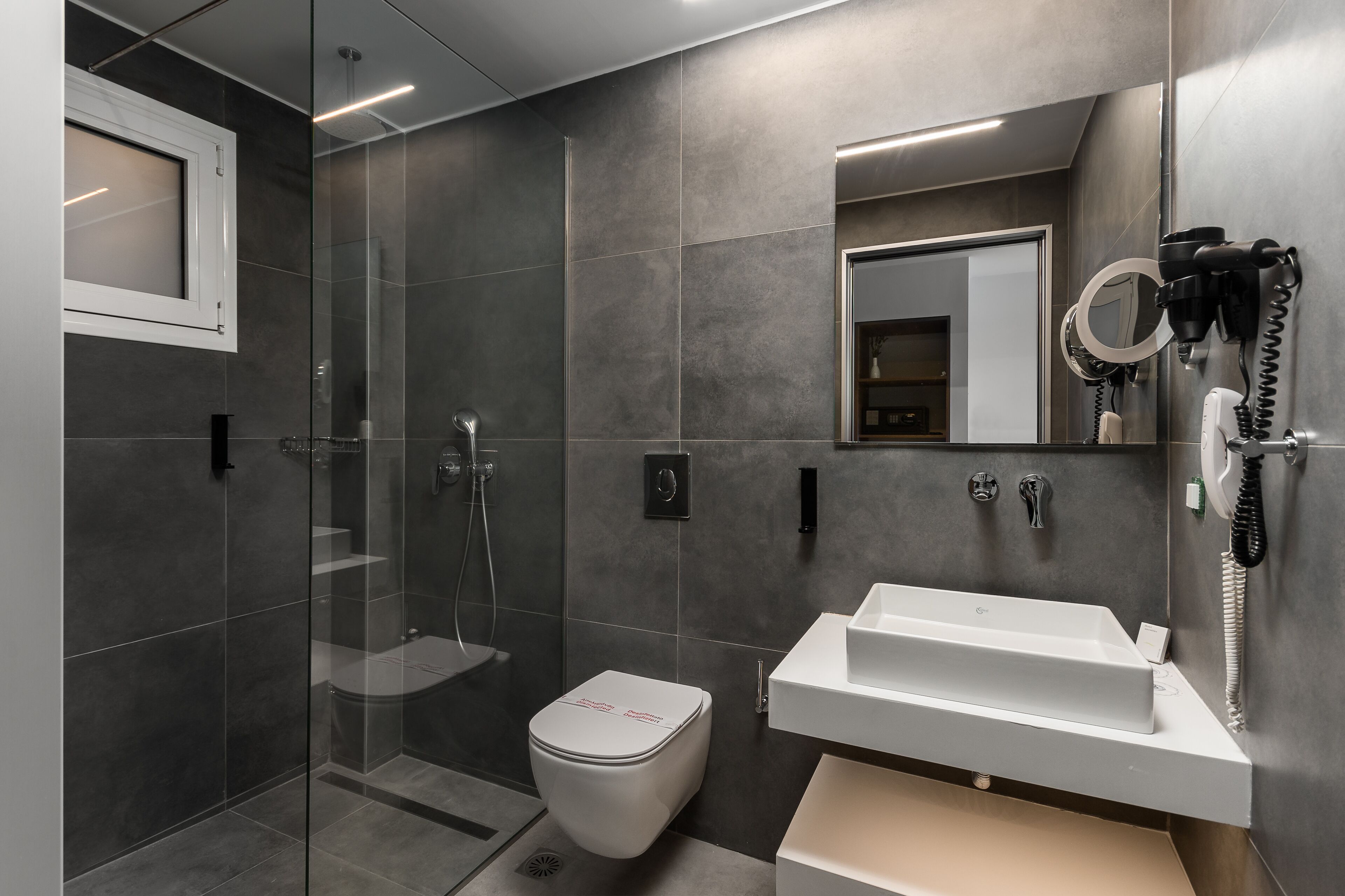 Een moderne badkamer met een douchecabine van glas, een toilet en een wastafel met een spiegel erboven.