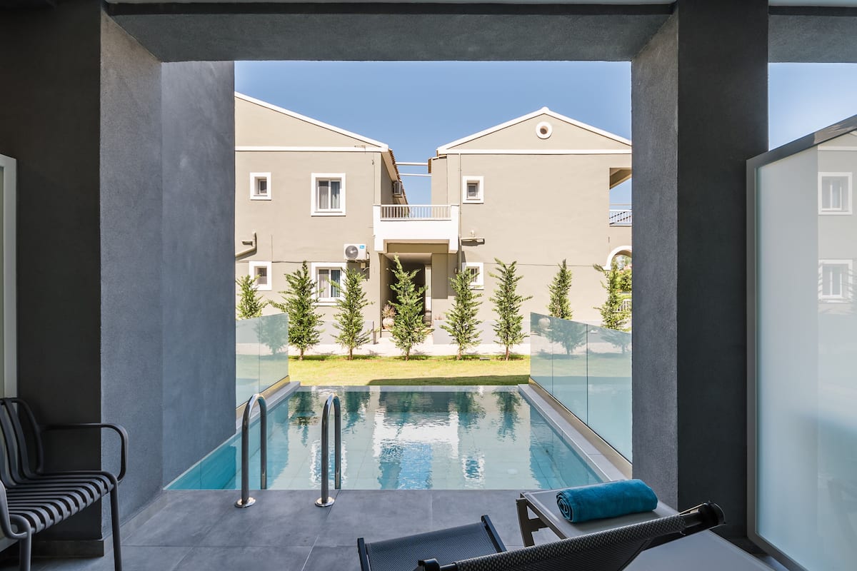 Ein moderner Poolbereich mit freiem Blick auf die angrenzenden Gebäude, eine Liege und ein kleiner Tisch mit einem Handtuch.