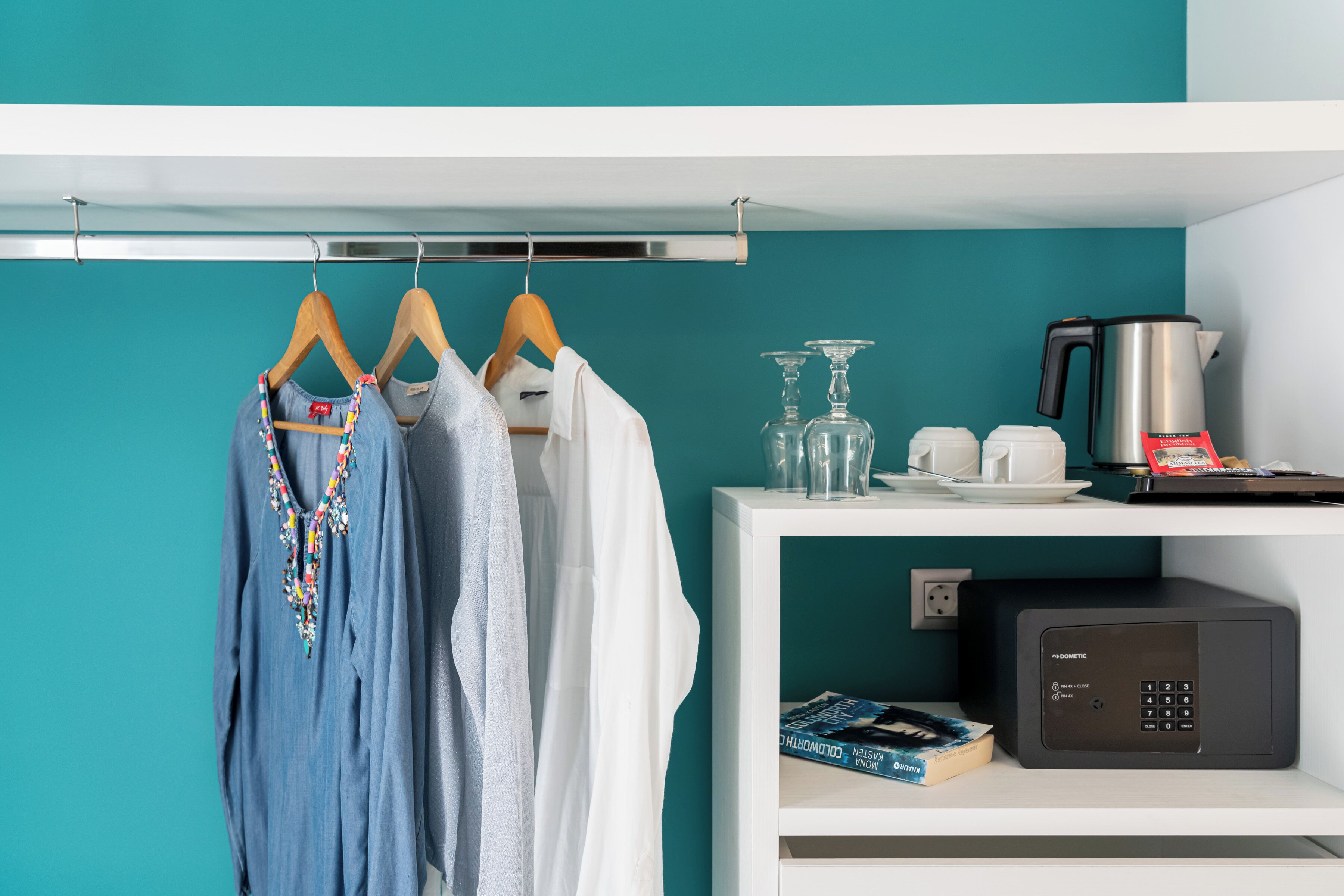 Un mur de couleur turquoise, une étagère blanche avec un four  à micro-ondes, une machine à café et un livre.