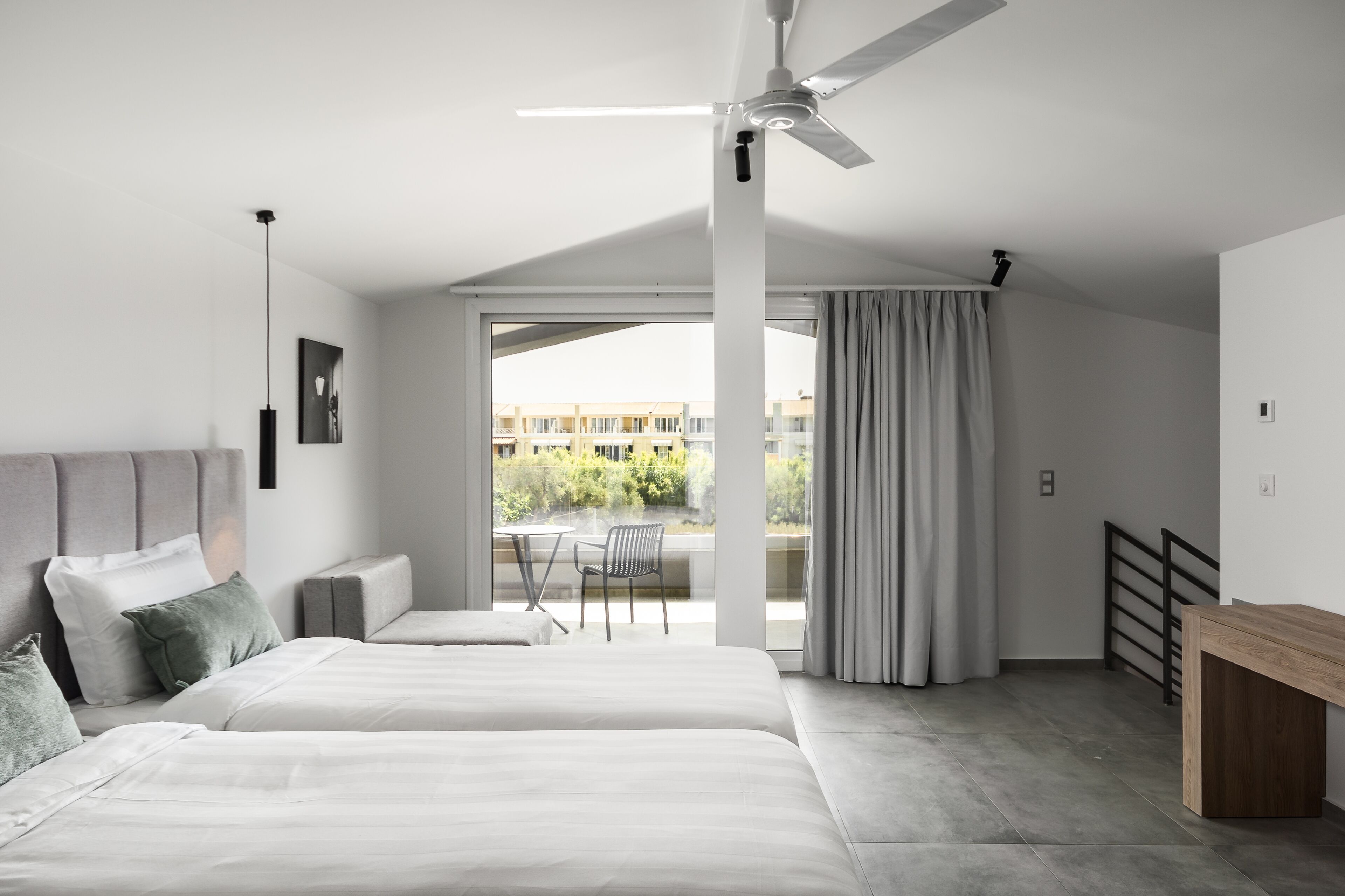Un dormitori modern amb un llit gran, un ventilador de sostre i vista a l'exterior.