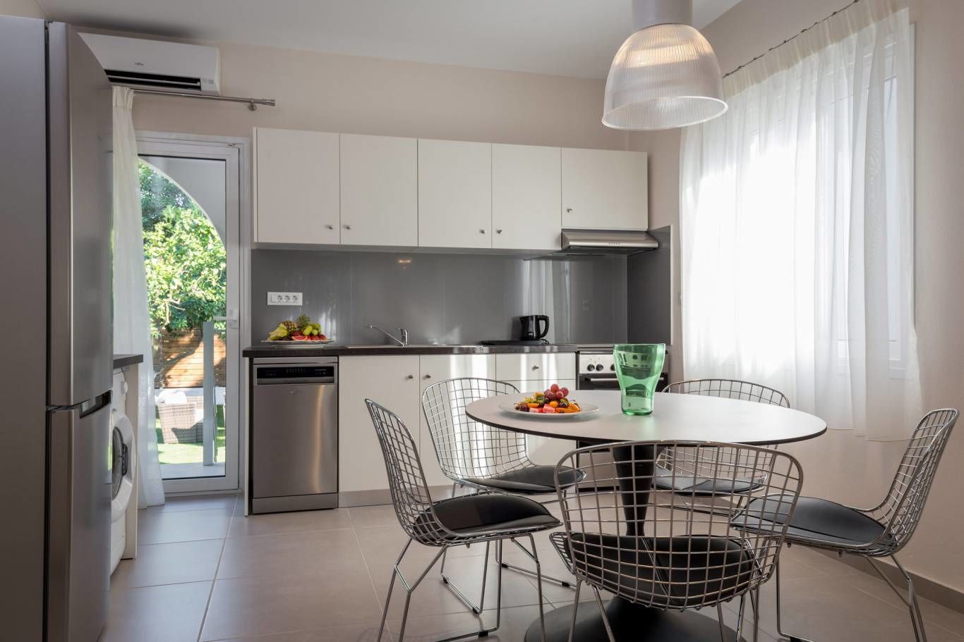 A modern kitchen with white cabinets, stainless steel appliances, and a dining area with wire chairs and a round table.