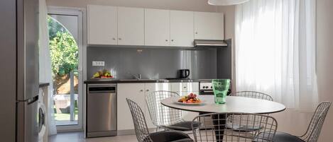 A modern kitchen with white cabinets, stainless steel appliances, and a dining area with wire chairs and a round table.