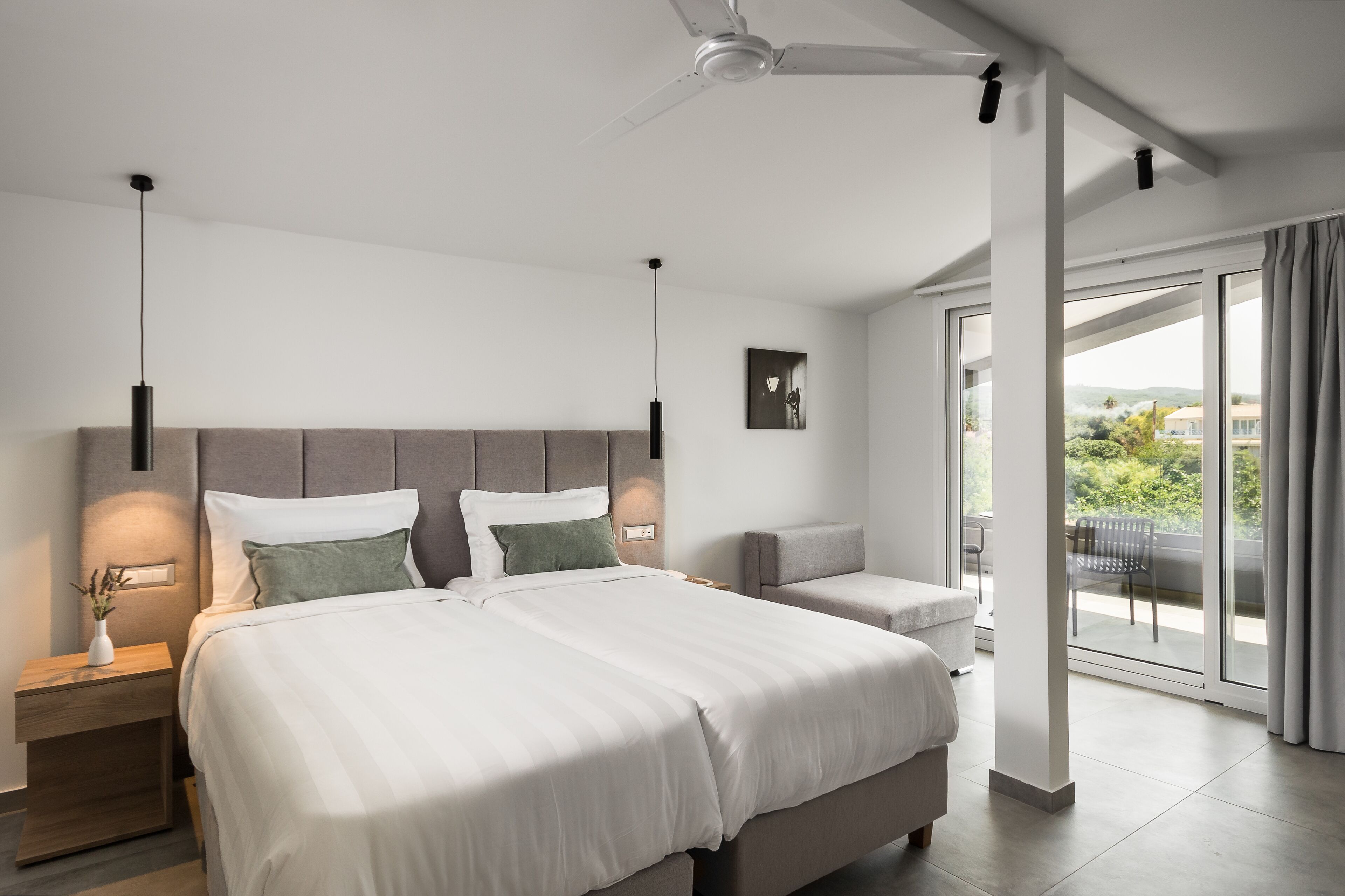 A modern bedroom with a large bed, bedside tables, a ceiling fan, and a balcony with a view.