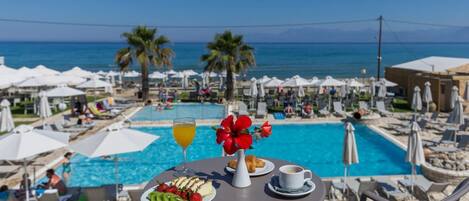 A poolside table with a fruit plate, a glass of orange juice, a cup of coffee, and a vase of red flowers.