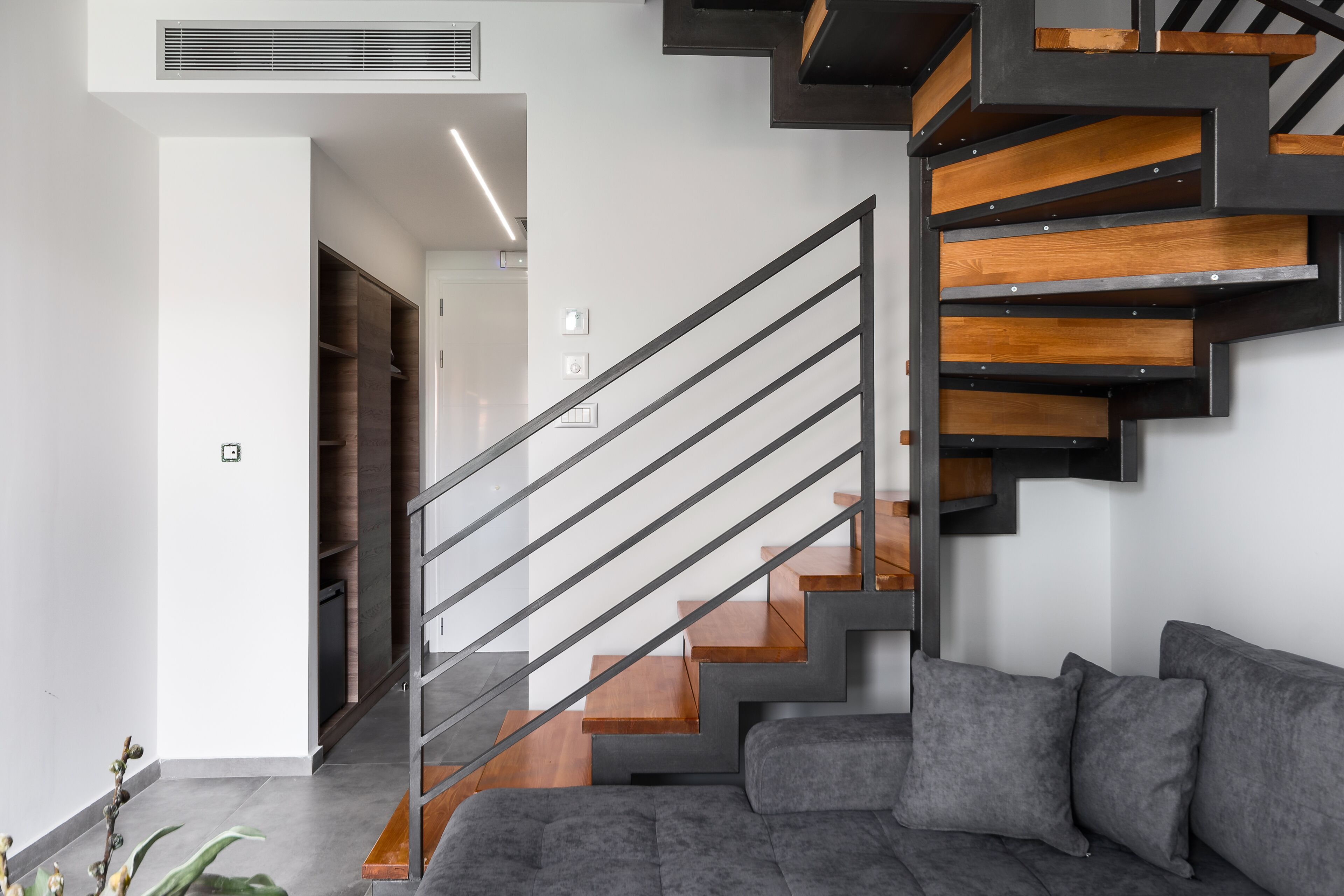 A modern staircase with wooden steps and metal railings, leading to a room with a grey sofa and a wooden door.