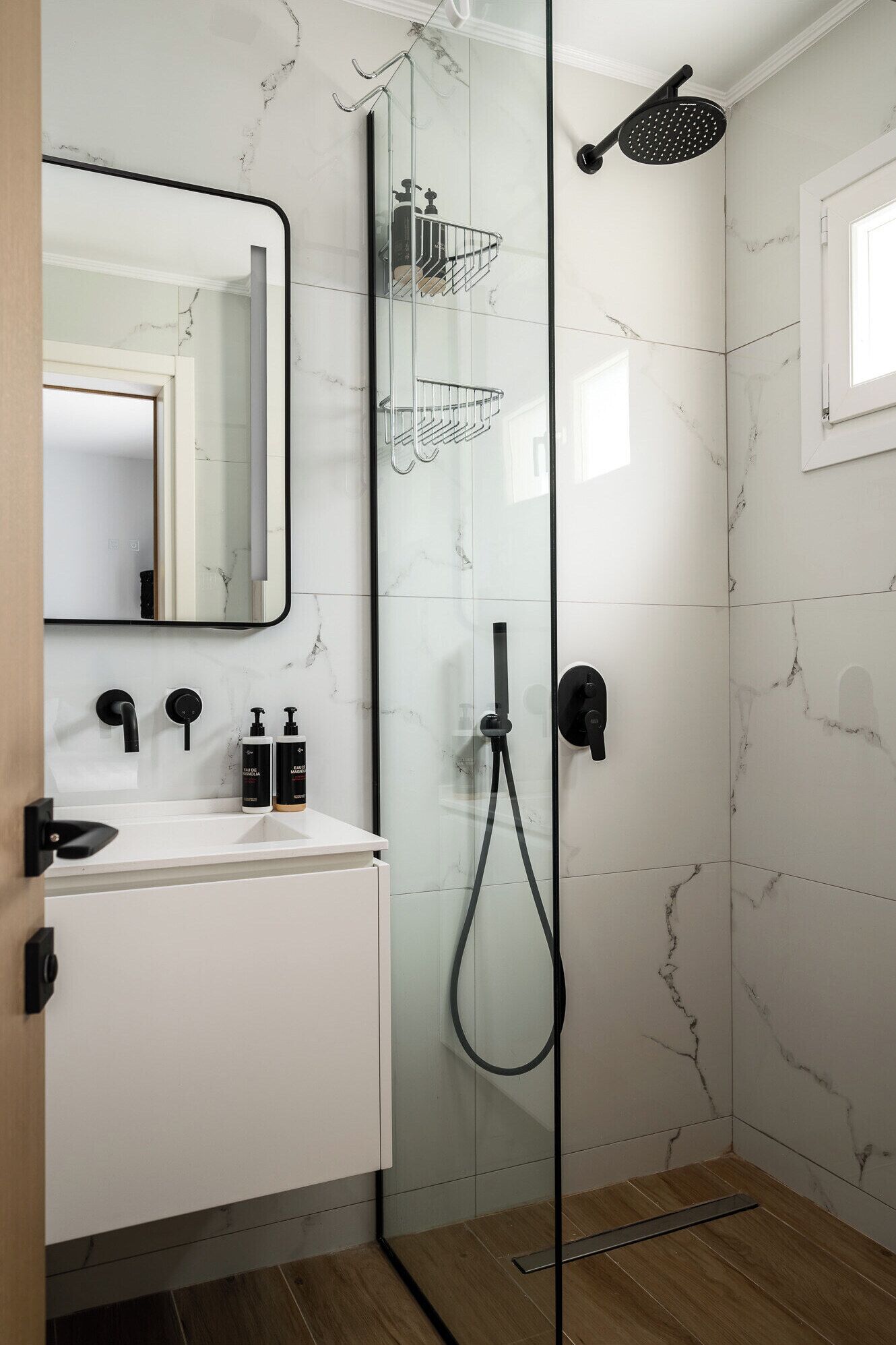 A modern bathroom with a glass shower enclosure, a white marble backsplash, and a large mirror above the sink.