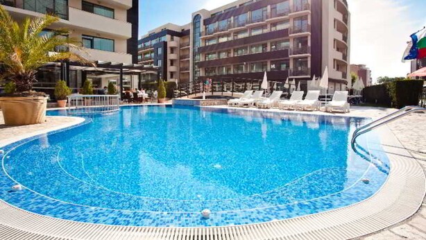A swimming pool with lounge chairs and umbrellas, surrounded by modern buildings.