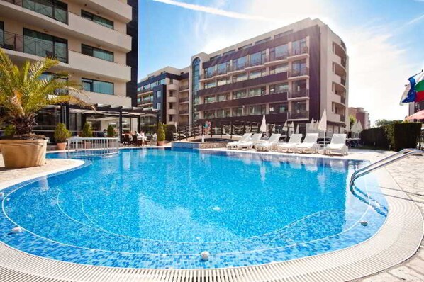 A swimming pool with lounge chairs and umbrellas, surrounded by modern buildings. - Hotel Lion Sunny Beach (Sunny Beach)