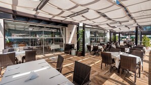 An outdoor dining area with wicker furniture and a glass wall overlooking a street.