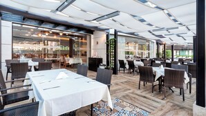 An indoor dining area with tables and chairs, large windows, and a ceiling with a unique design.